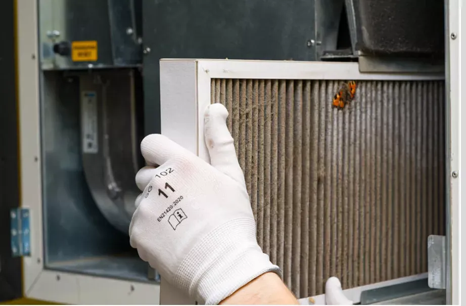 Gloved hand removing a dirty HVAC air filter