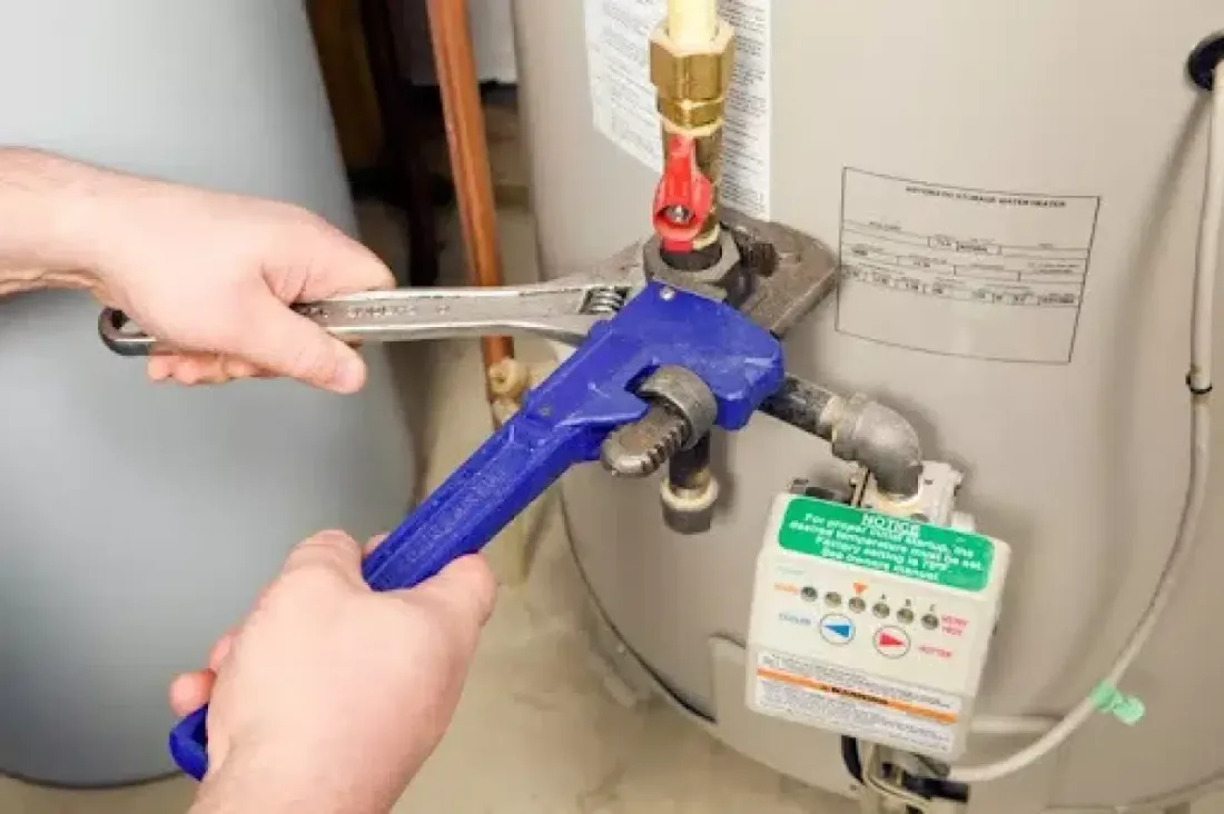 Hands using wrenches on a water heater connection
