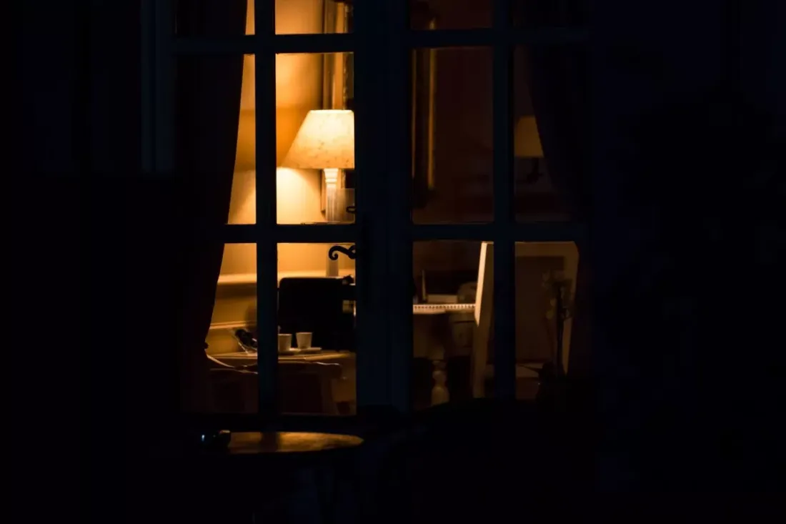 Lamp lighting a room at night, seen through a window