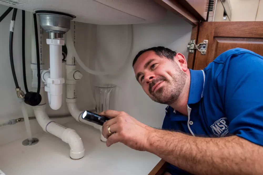 MSP plumber inspecting pipes under a sink