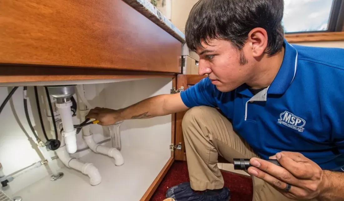 MSP plumber repairing drain pipes under a sink