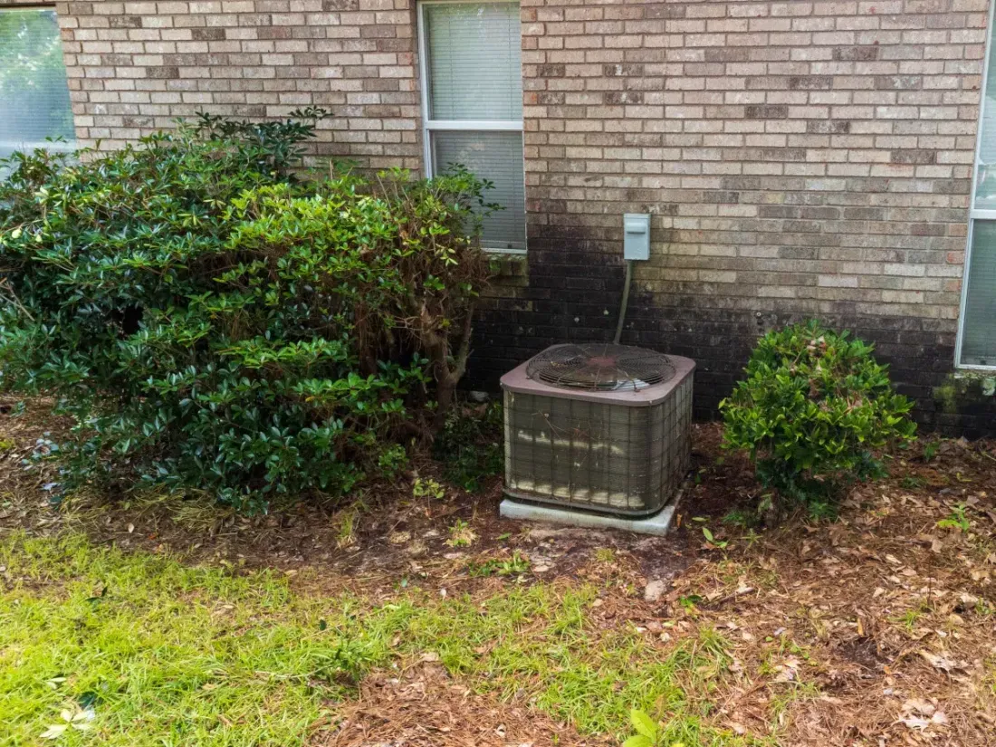 Outdoor air conditioner beside brickwork and shrubs