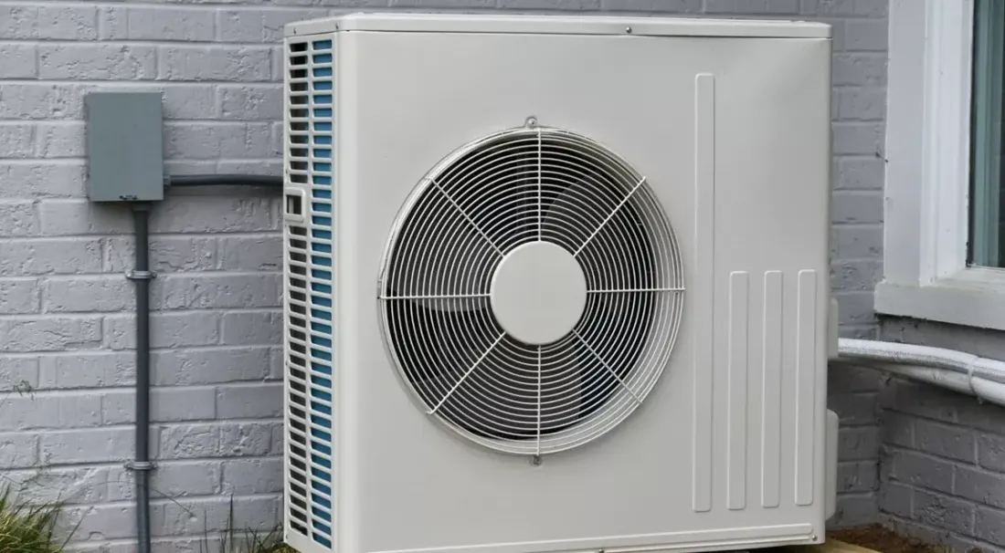 Outdoor heat pump mounted beside a brick wall