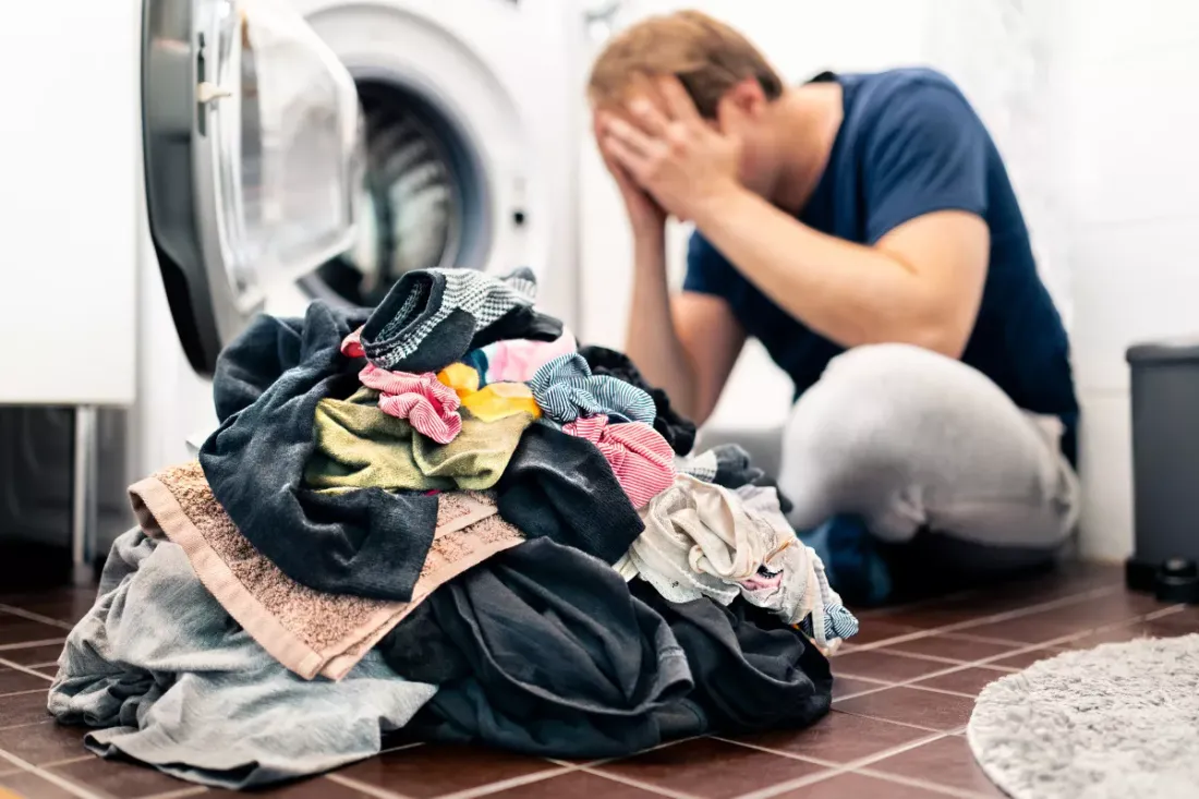 Person sitting beside a washing machine and a pile of laundry