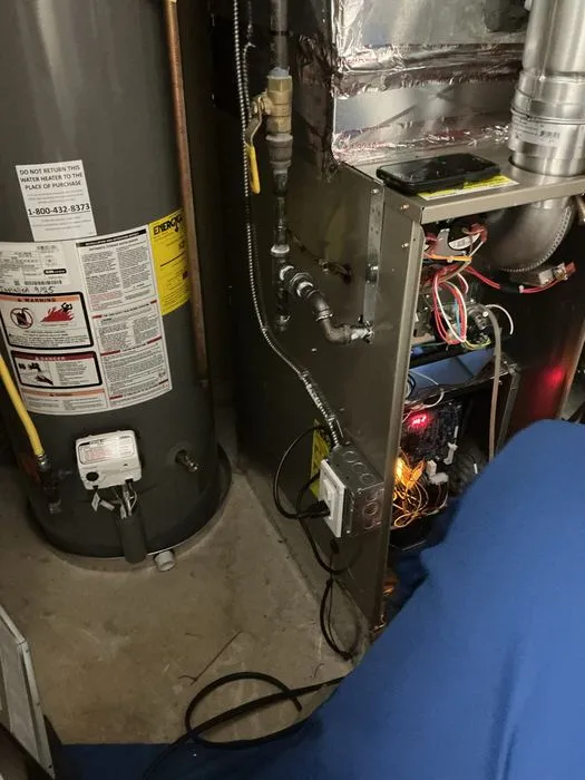 Technician inspecting an open furnace beside a water heater
