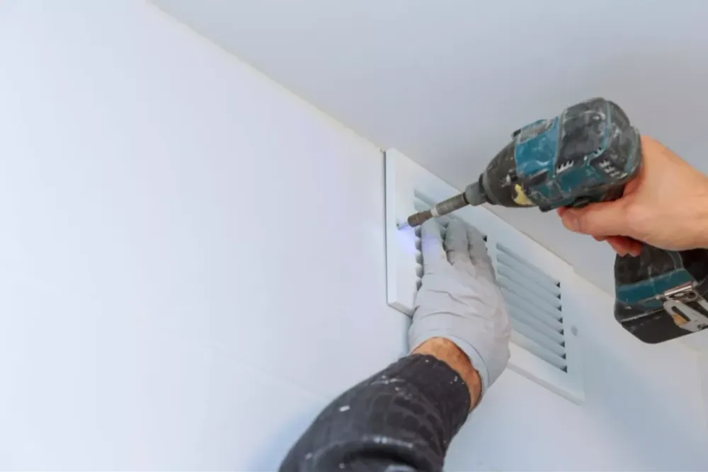 Technician using a drill on a wall air vent