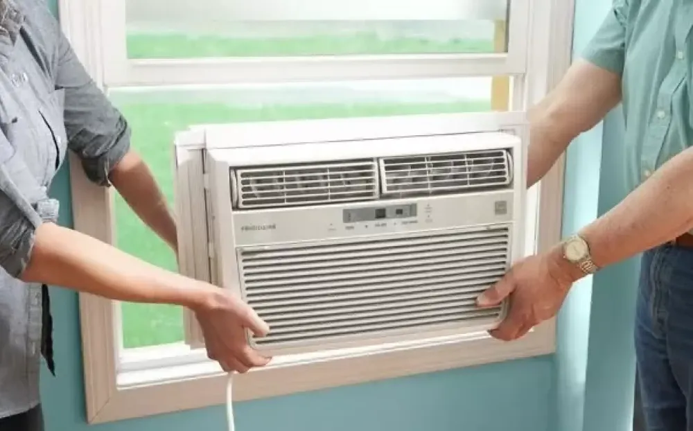 Two people fitting an air conditioner into a window