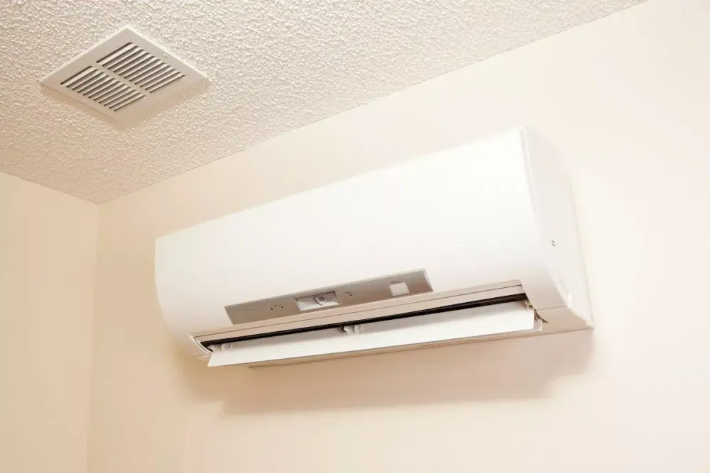 Wall-mounted ductless indoor unit below a ceiling vent