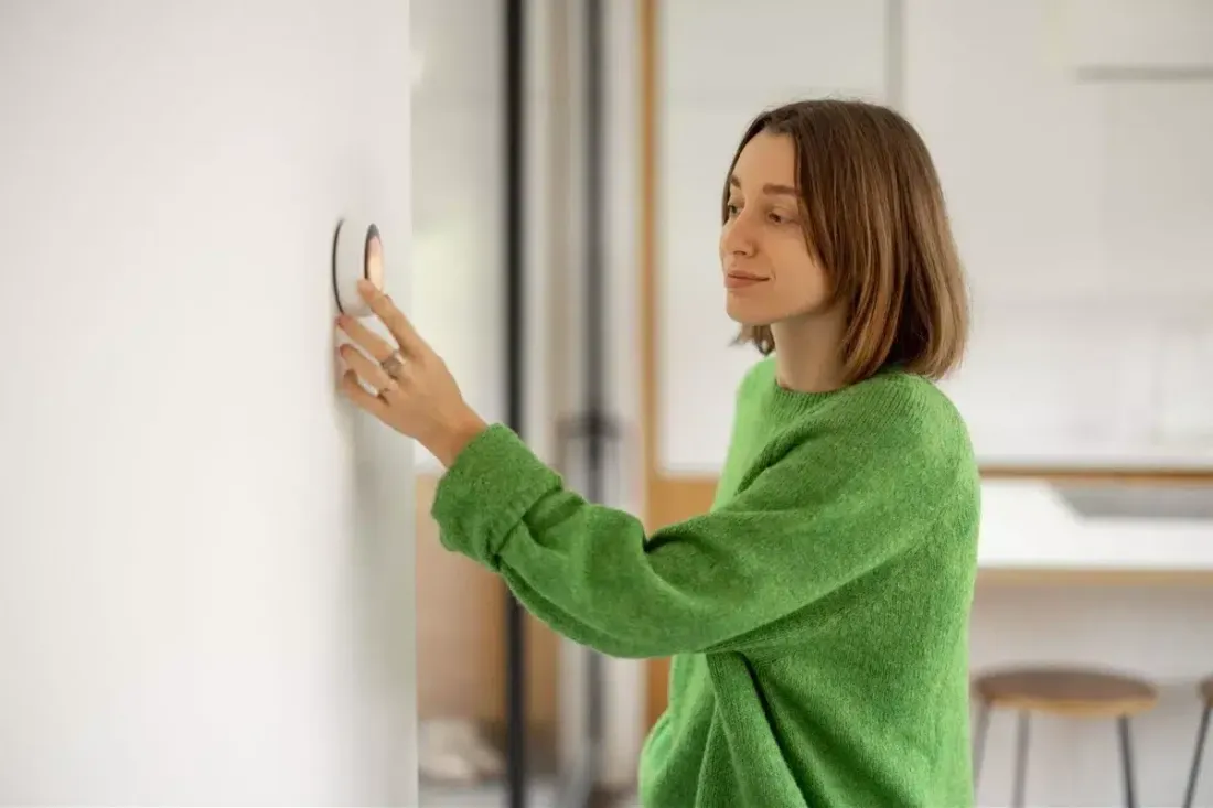 Woman adjusting a thermostat while wearing a green sweater