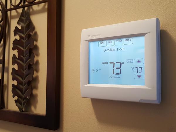 White Honeywell thermostat affixed to a beige colored wall and that is displaying 73 degrees on it's lit up LCD screen.