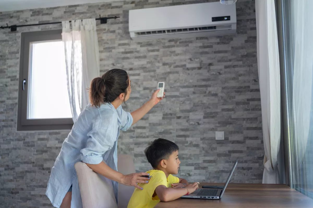 a women adjusting Air conditioner with a child sitting on a chair besides her