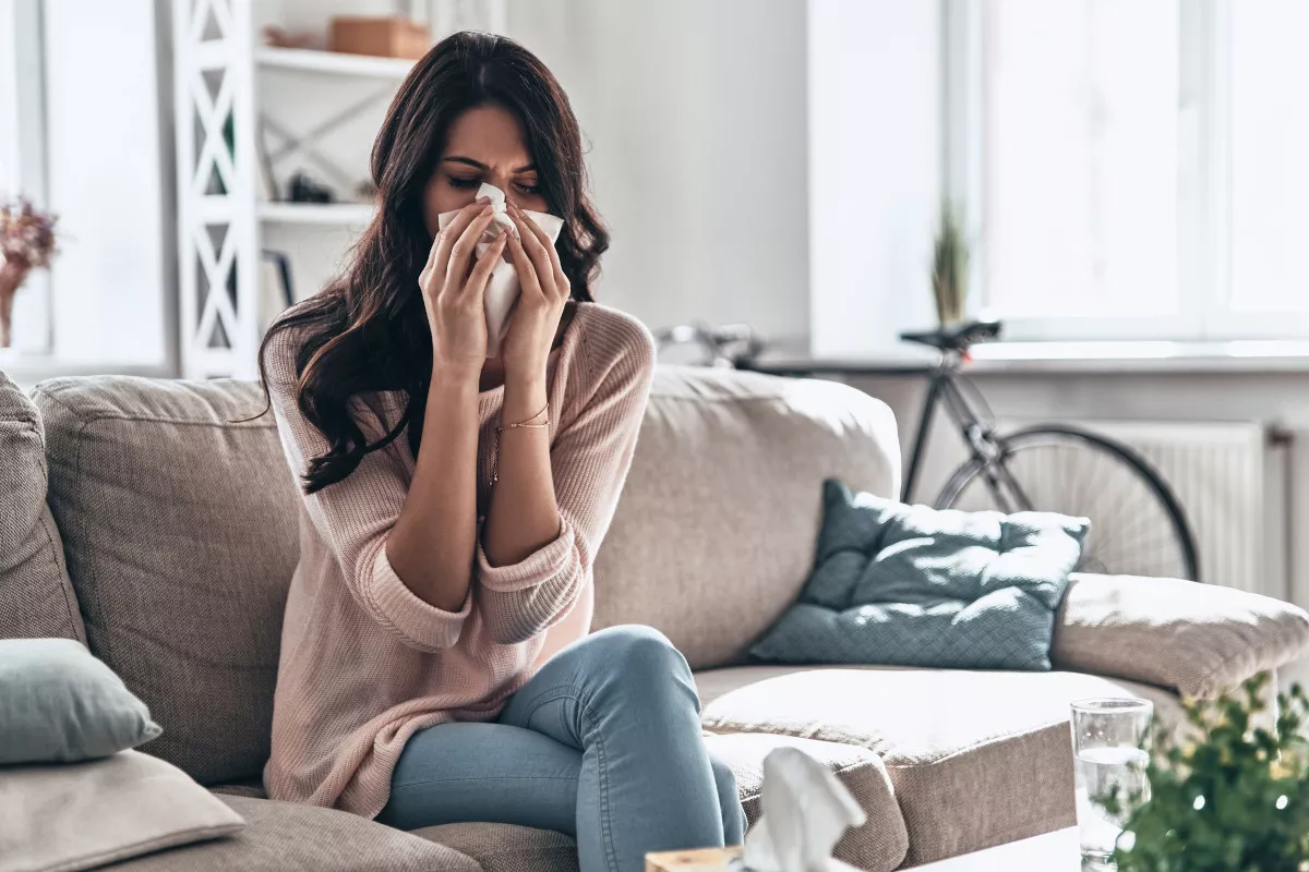 Woman sitting on sofa wiping her nose