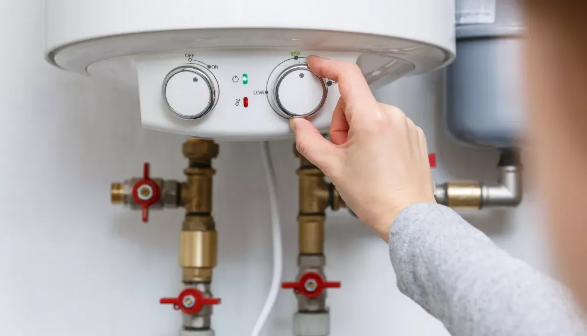 A hand on water heater adjusting heater temperature